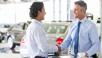 Two men shaking hands at an auto dealership.