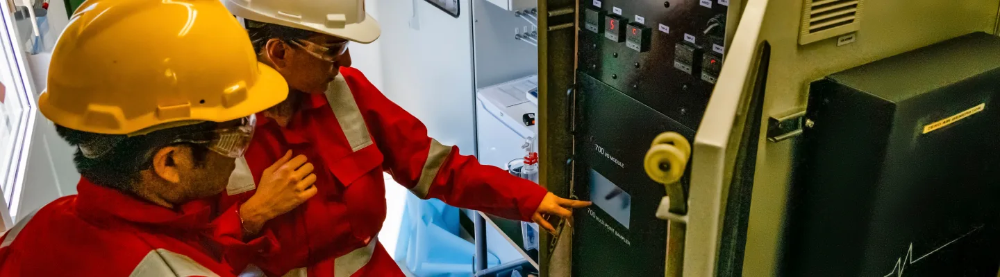 Two workers in red protective suits and helmets examining an electrical panel in an industrial environment