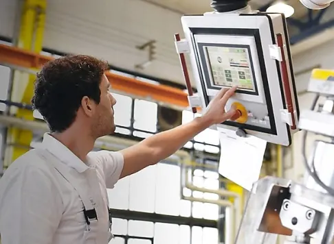 An operator in a manufacturing facility using a touchscreen control panel to manage machinery