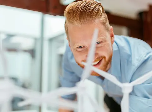 A smiling professional examining a model of wind turbines in a bright office environment.