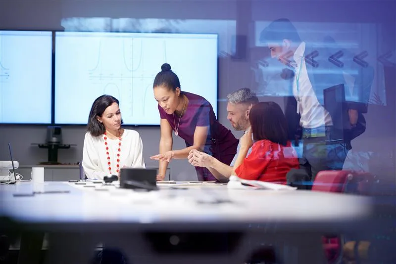 A team of professionals collaborating in a modern conference room, with screens displaying visuals in the background.