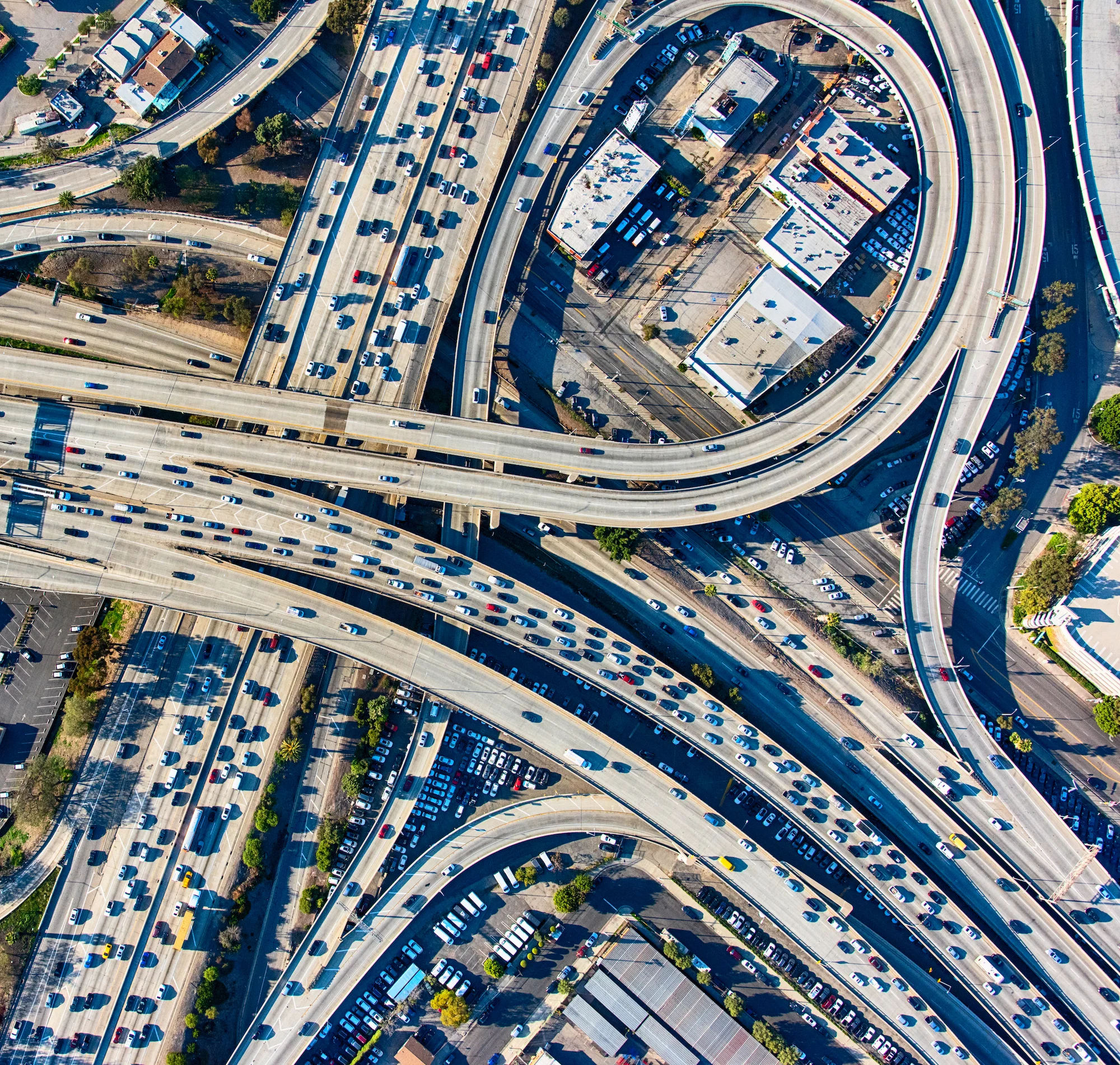 An aerial view of a complex highway interchange with multiple lanes of traffic, bridges, and ramps weaving through an urban area.