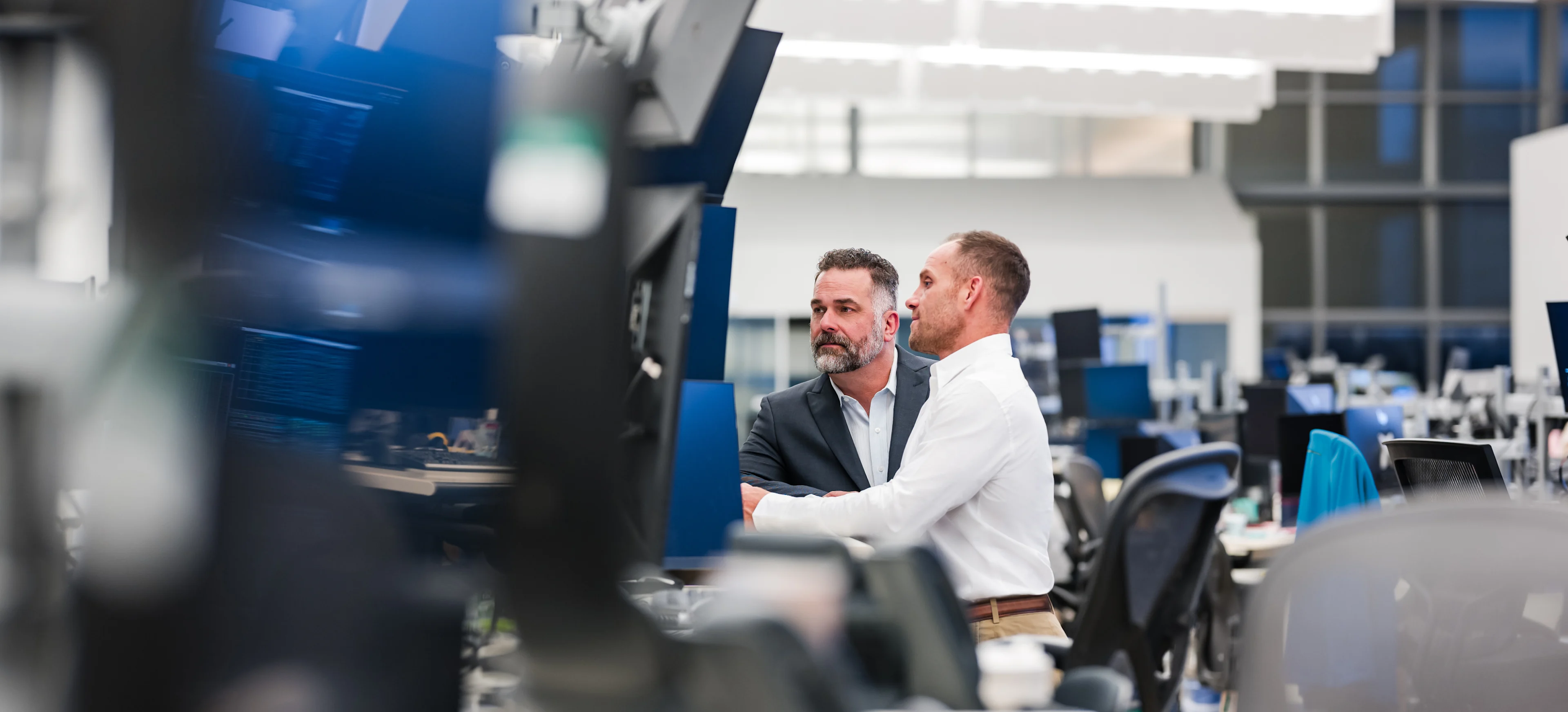 Two men working in an office with many monitors